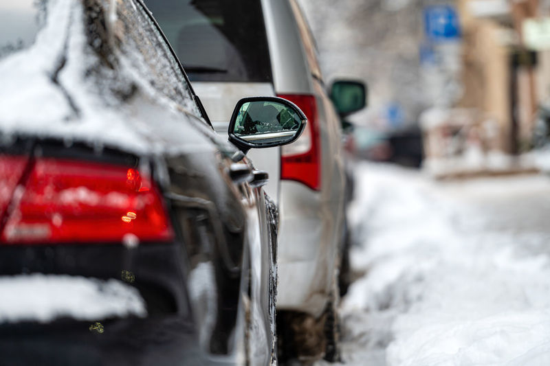 Cars parked on snowy street, rear side view, selective focus on rear view mirror