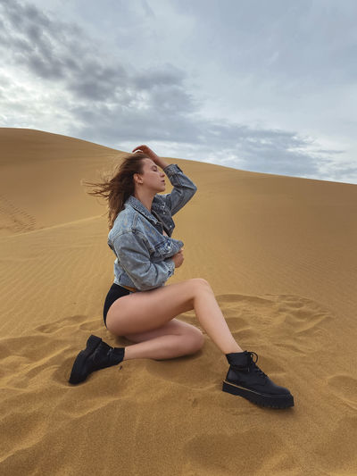 Yong woman sitting on sand at desert