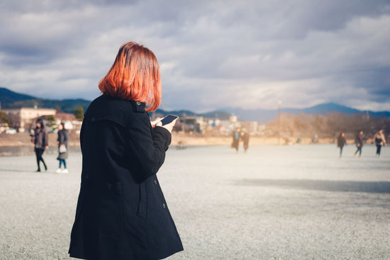 Woman using mobile phone against cloudy sky