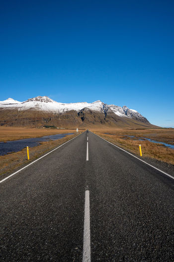 Road leading towards mountains against clear blue sky