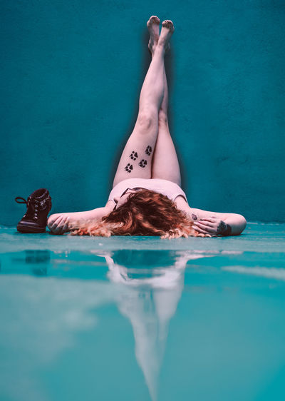 Young woman with feet up lying on turquoise wet floor