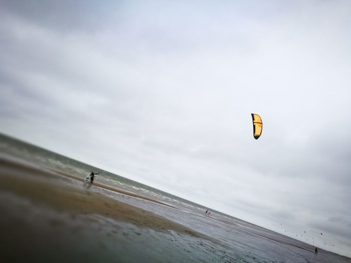 Person paragliding over beach against sky