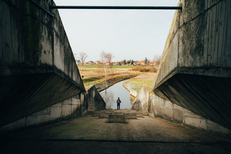 Full length rear view of man standing by canal against sky
