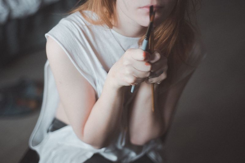 Close-up midsection of teenage girl holding paintbrushes while sitting at home