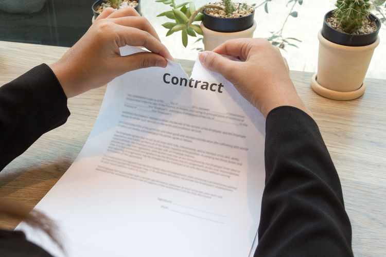 Cropped hands of businesswoman tearing contract at desk