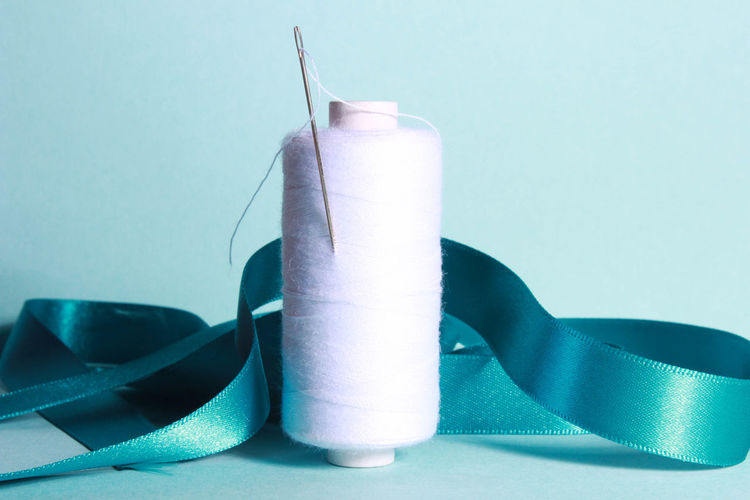 Close up of thread spool with ribbon and needle over blue background