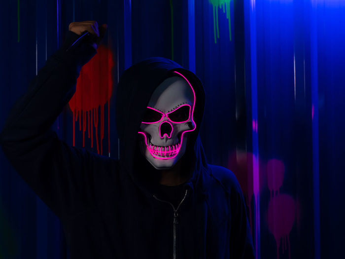 Serial killer wearing neon skull mask  at halloween costume party with colorful background.