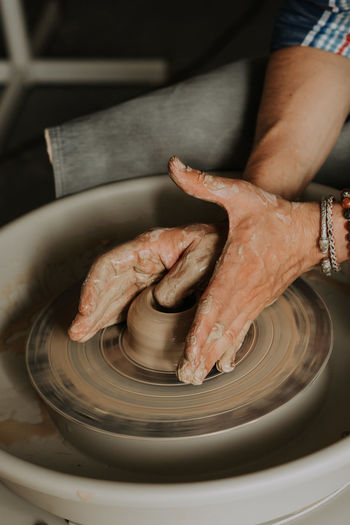 Close-up shot of ceramic cup spinning on potters's wheel and hands molding clay