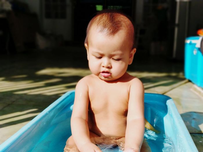 Close-up of cute shirtless baby boy sitting in wading pool
