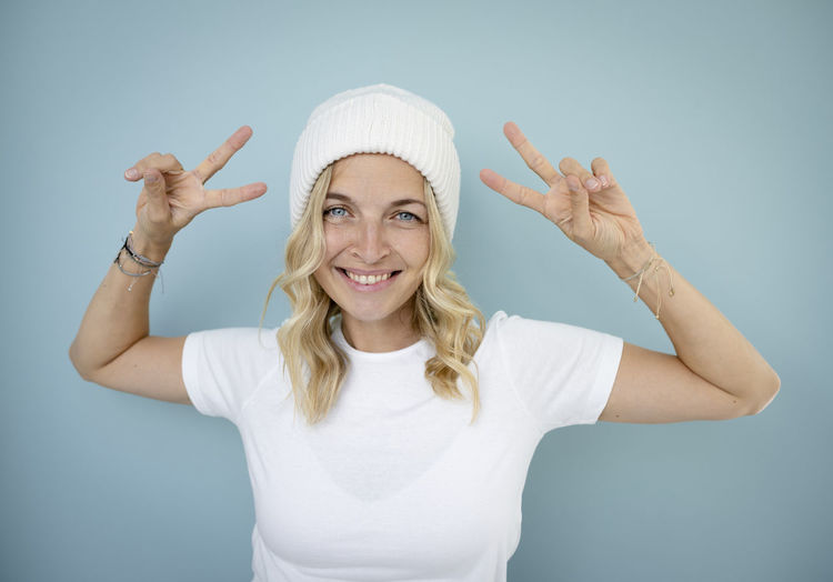Portrait of smiling young woman wearing hat against wall