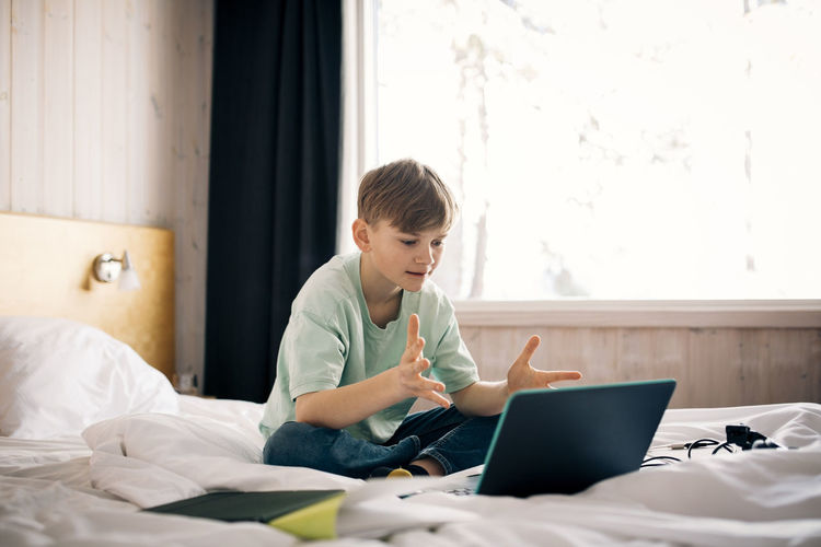 Boy attending video call while gesturing during homeschooling in bedroom