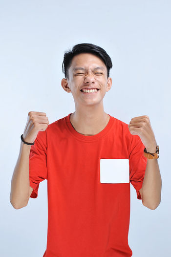 Young asian man happy and excited expressing winning gesture. successful and celebrating