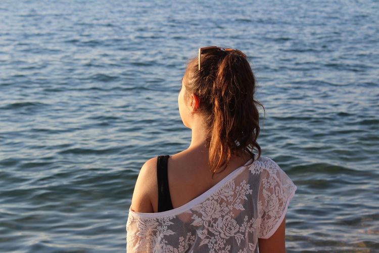 Rear view of young woman standing against sea