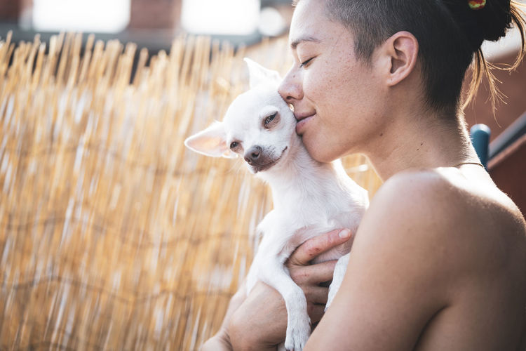 Beautiful woman and tiny dog smile and embrace in afternoon sun