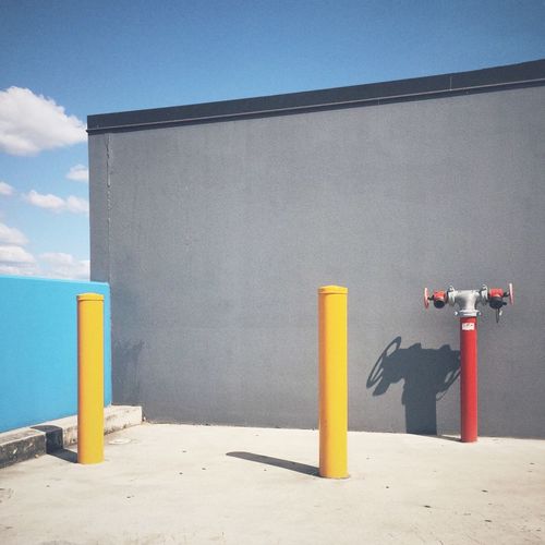 Bollards and fire hydrant by gray wall against sky