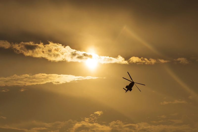 Low angle view of silhouette helicopter flying against sky during sunset