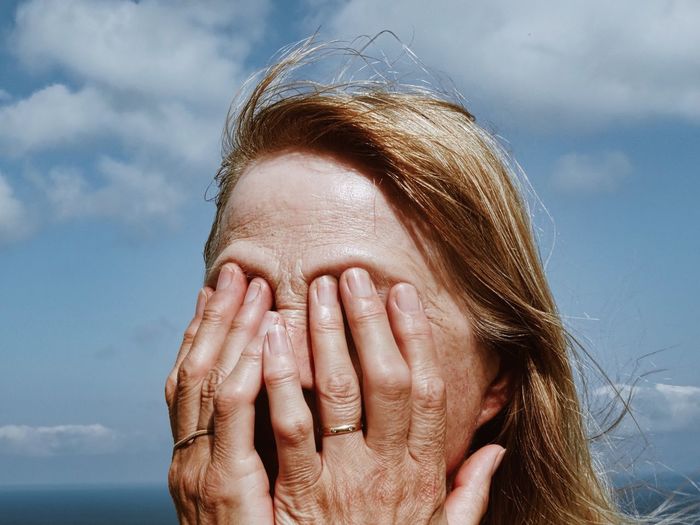 Close-up of woman covering eyes against sky