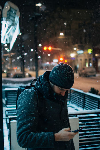 Man using phone during snowfall at night