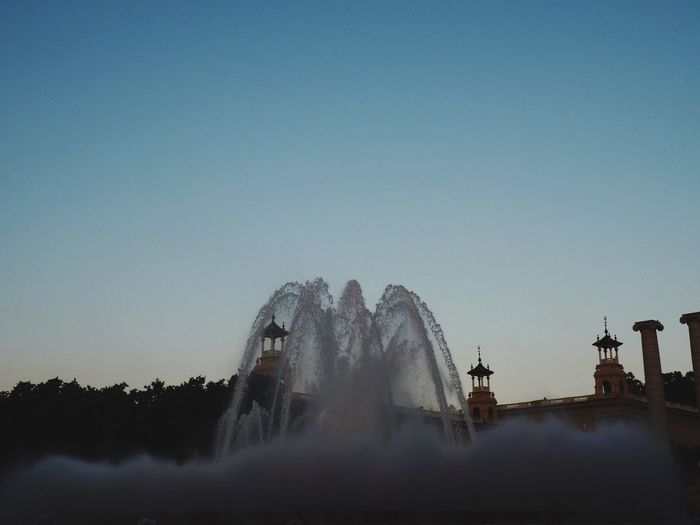 Low angle view of magic fountain outside national palace against clear blue sky at dusk