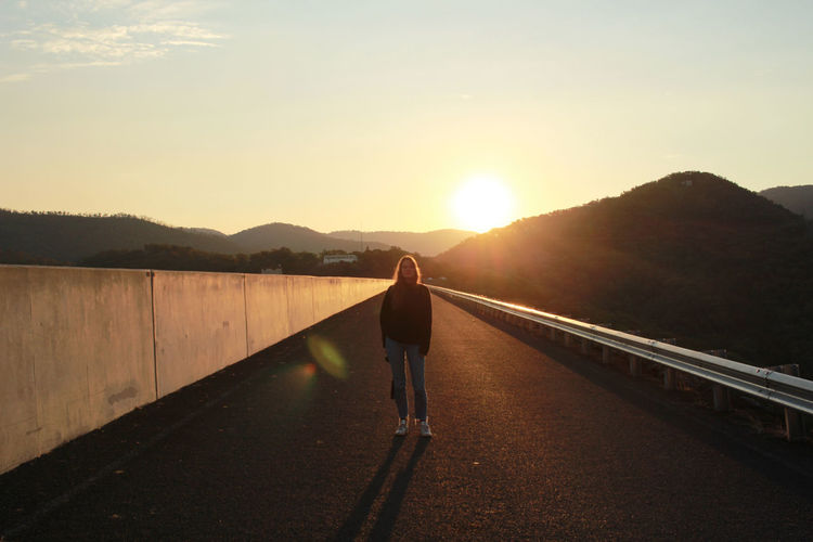 Full length of woman standing on road against sky during sunset