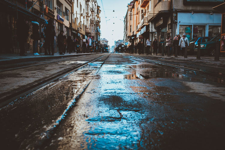 Wet street amidst people walking on footpath in city