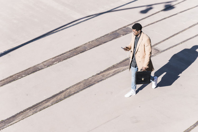 Businessman walking outdoors with briefcase, cell phone and earphones