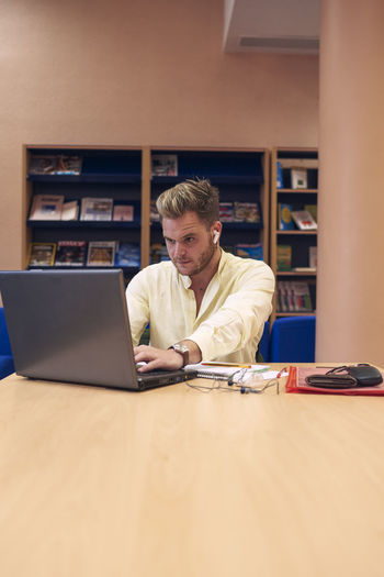 A young boy sitting and working with his laptop in the library