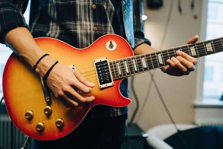 Midsection of man playing guitar while rehearsing in recording studio