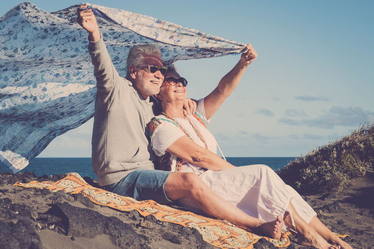 Senior couple holding scarf while relaxing at beach