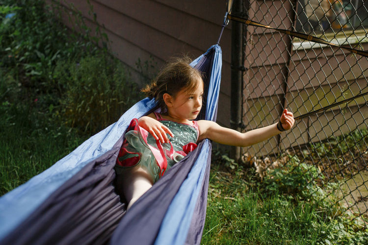 A small girl in a bright colored tutu plays in a hammock in sunshine