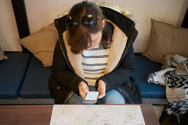 Woman sits looking at her phone in front of a tourist map person