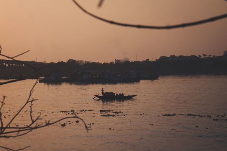 Silhouette boat in river against sky during sunset