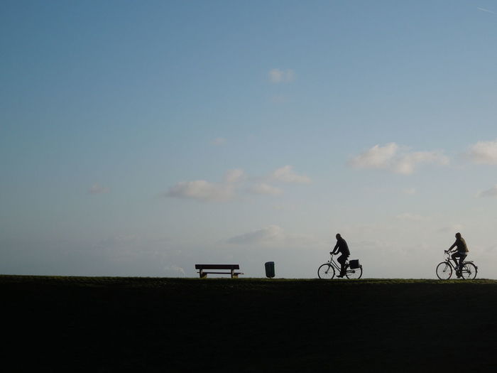Side view of bicycling on landscape against sky