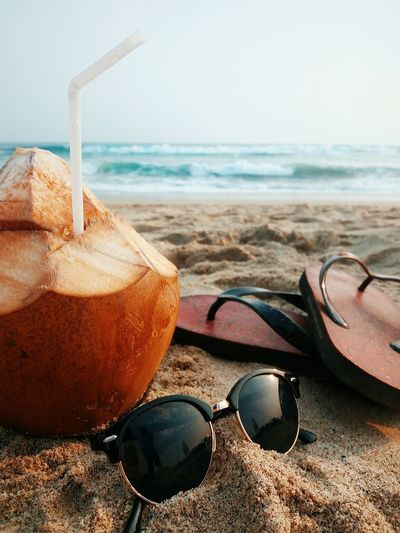 Close-up of coconut by sunglasses and flip-flops at beach
