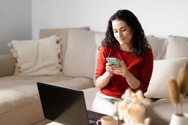 Young woman using digital tablet while sitting on sofa at home