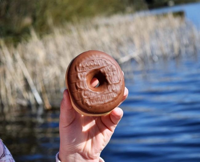 Close-up of hand holding donut against water