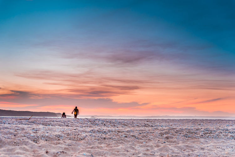 Silhouette people on beach against sky during sunset