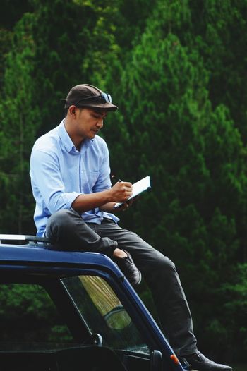 Full length of man writing on diary while sitting on car