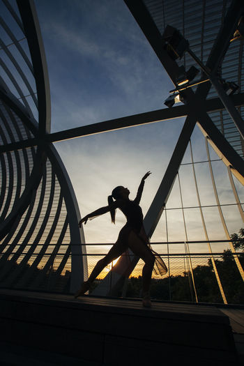 Ballerina dancing on bridge against sky during sunset
