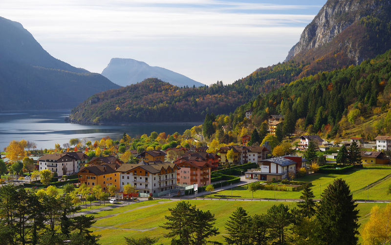 Scenic view of town and mountains by river against cloudy sky