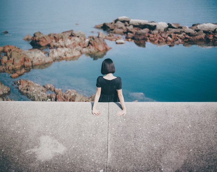 High angle view of woman standing by retaining wall against sea