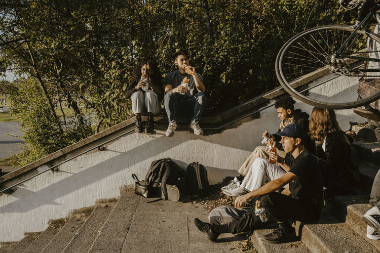 Friends having food and drink while sitting on steps in park