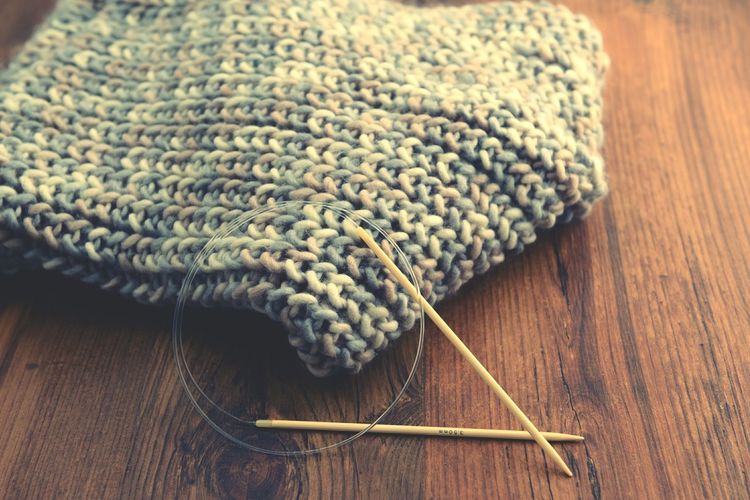 Knitting needles with scarf on wooden table