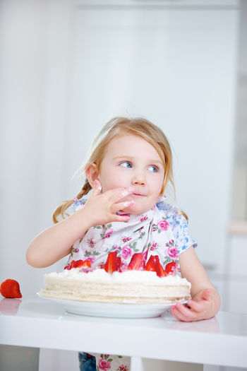 Cute girl looking away while eating cake at home