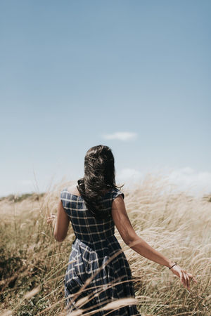 Rear view of woman walking on grassy field against sky