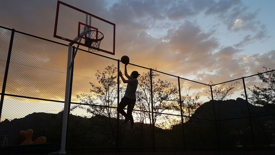 Silhouette man playing basketball against sky during sunset