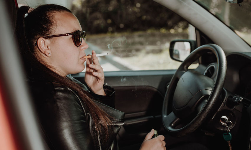 Portrait of young woman holding cigarette in car