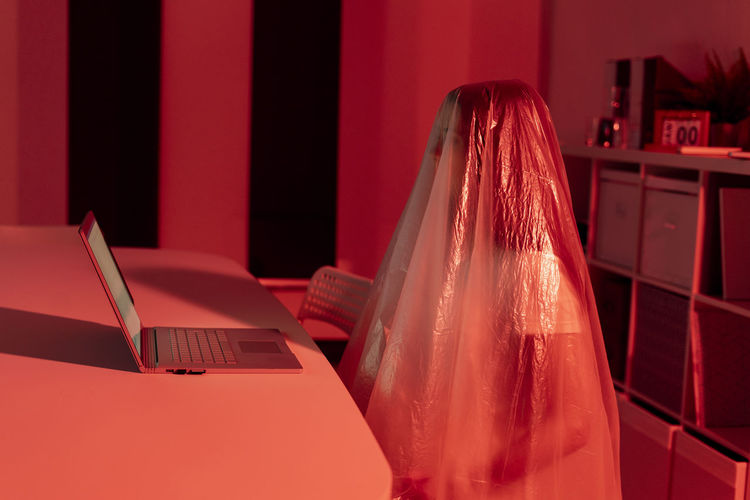 Young woman covered in plastic sitting with laptop at desk in home office during pandemic