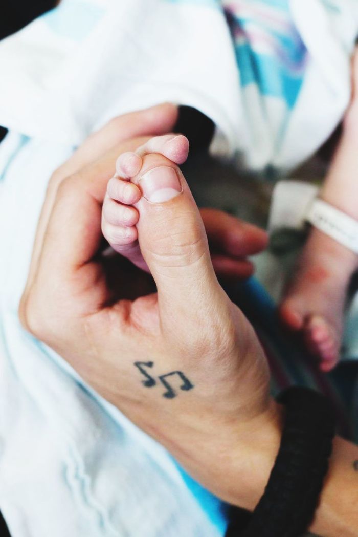 Cropped hand of parent holding toddler daughter foot on bed in hospital