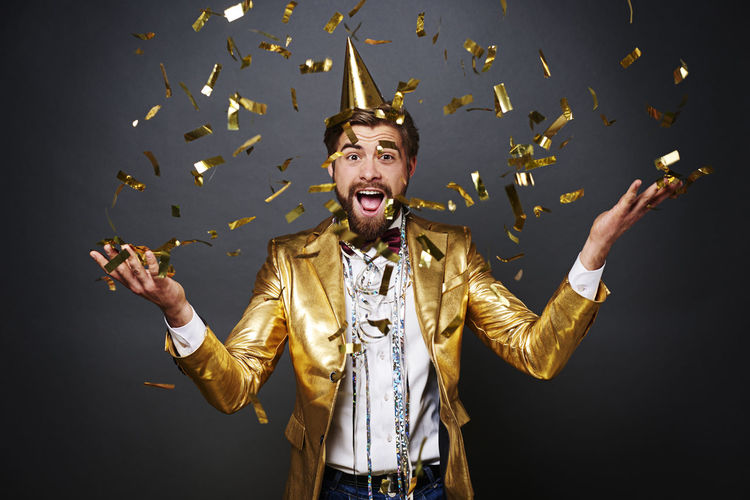 Portrait of happy young man throwing confetti while standing against black background